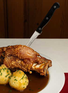 Schweinshaxe mit eingestecktem Messer, zwei Kartoffelknödeln mit Schnittlauch und dunkler Soße