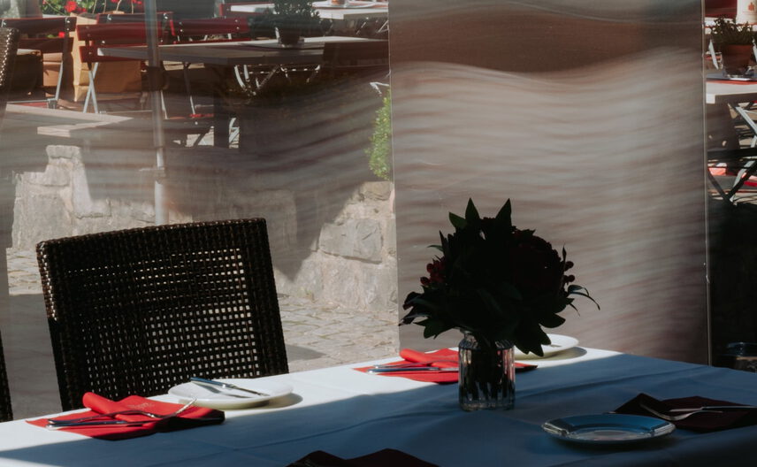 Weiß gedeckte Tafel mit roten Servietten und Blumen vor einem Werbeaufsteller mit Kunstflugzeugen im Freien