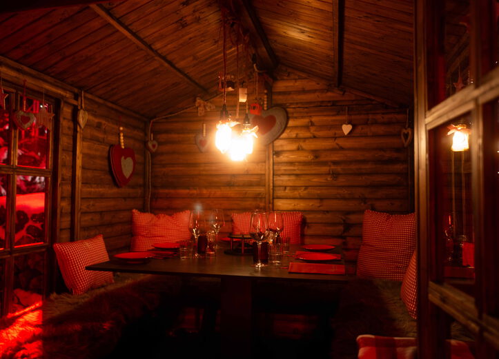 Gemütliche Holzhütte mit gedecktem Tisch, rot karierten Kissen, Fellen und Herzdekoration im warmen Licht
