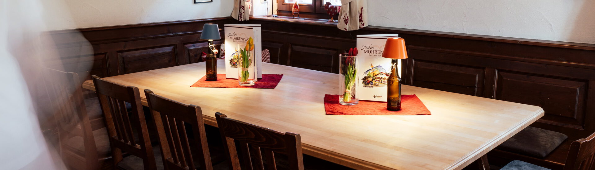 Großer Holztisch mit Tulpen, Tischlampen und Speisekarten „Fischers Mohrenplatz“ in einer getäfelten Gaststube
